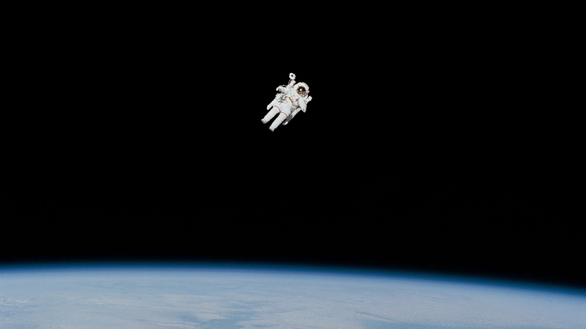 A person in a spacesuit floating in space, a small piece of Earth is at the bottom of the photo